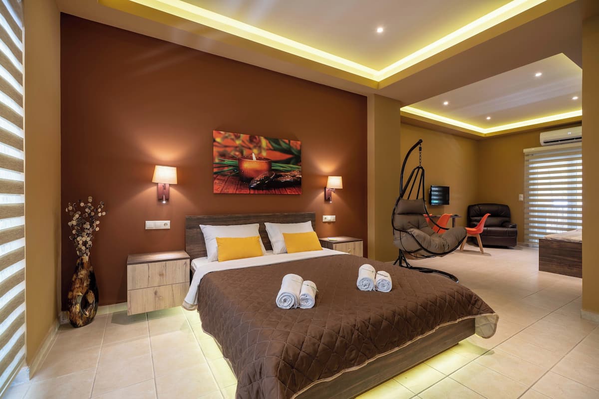 Une chambre moderne avec un grand lit, deux lampes de chevet, un téléviseur fixé au mur et un fauteuil suspendu.