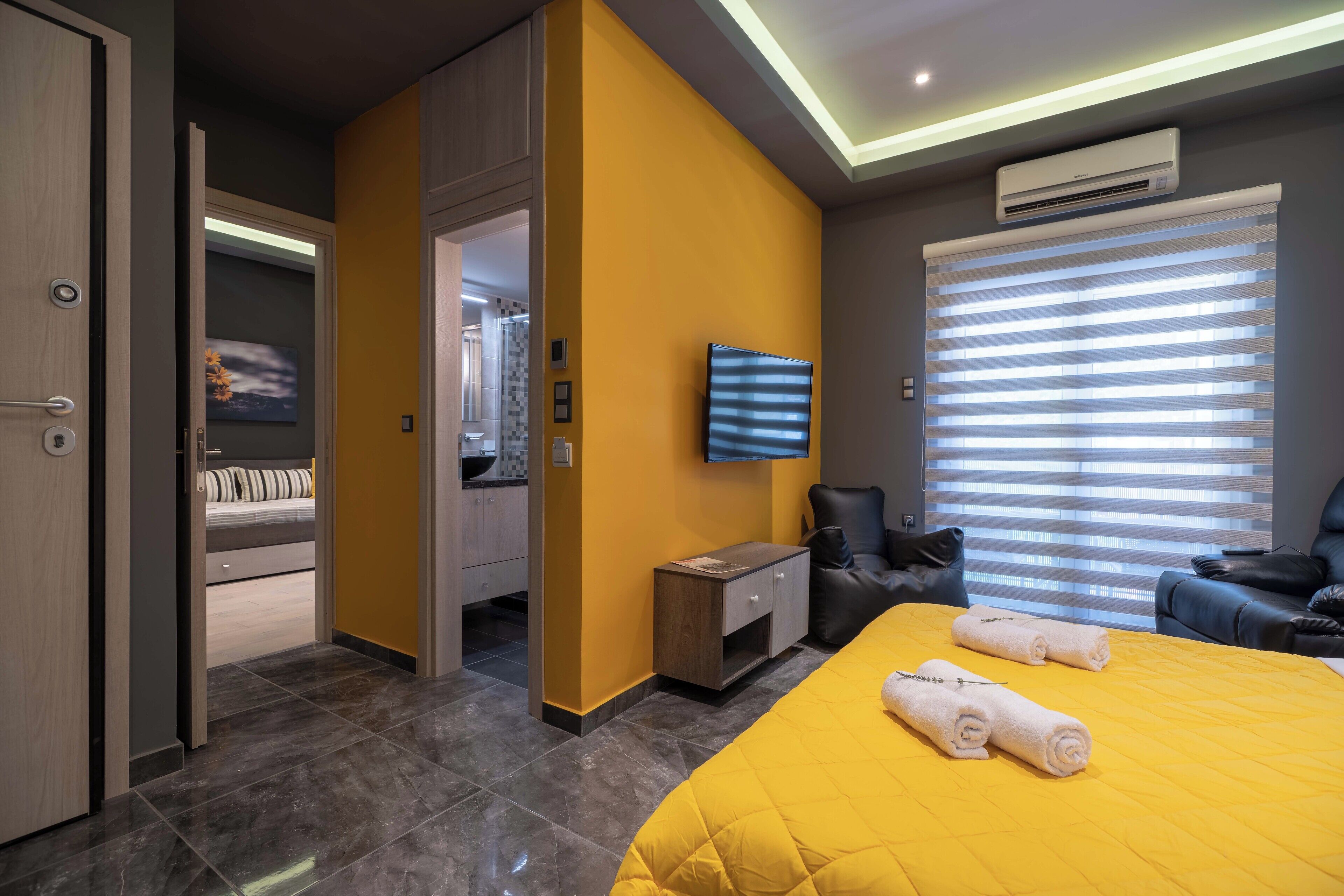 A hotel room with a bed, a TV, a seating area, and a bathroom visible through an open door.