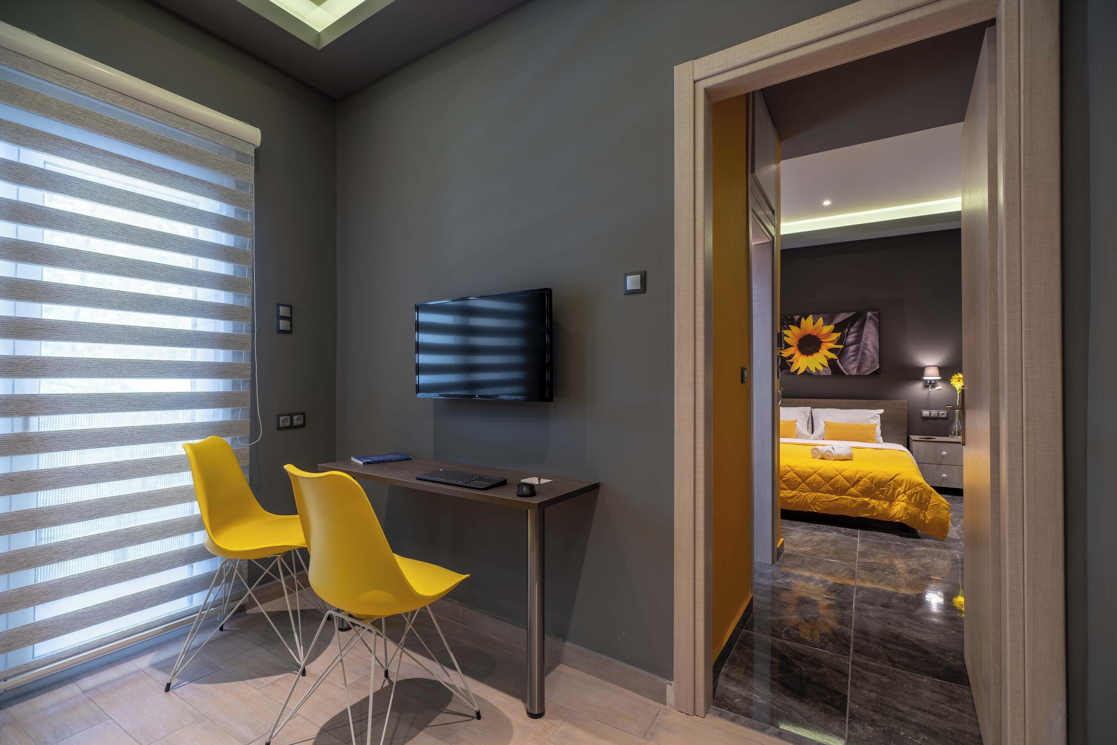Habitación de hotel moderna con escritorio, dos sillas amarillas, televisor de pantalla plana y cama con colcha amarilla.