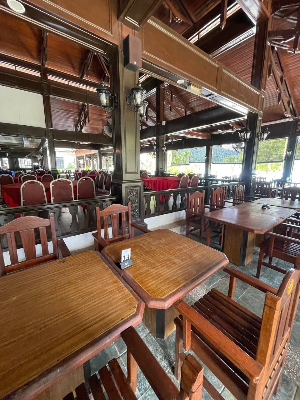 A restaurant with wooden tables and chairs, large windows, and a high ceiling with exposed beams.