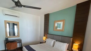 Une chambre d’hôtel équipée d’un lit, d’un bureau, d’une chaise, d’un ventilateur de plafond, d’un climatiseur mural et d’une lampe de chevet.