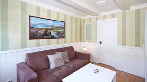Ein Zimmer mit einem braunen Sofa, einem weißen Couchtisch, einem gerahmten Landschaftsbild und einer Tür mit einem Spiegel.