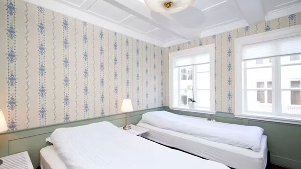 Ein Hotelzimmer mit zwei Einzelbetten, einem kleinen Tisch und einer Lampe.