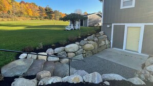 Una propiedad residencial con un muro de piedra, un patio cubierto de césped y una casa con puerta amarilla.