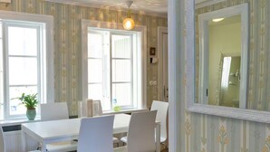 A dining area with a white table and chairs, a hanging light fixture, and a mirror with a decorative frame.