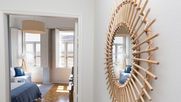 Une chambre d’hôtel moderne avec un grand miroir, un lit avec une literie bleue, un plancher en bois et une vue sur la ville par la fenêtre.