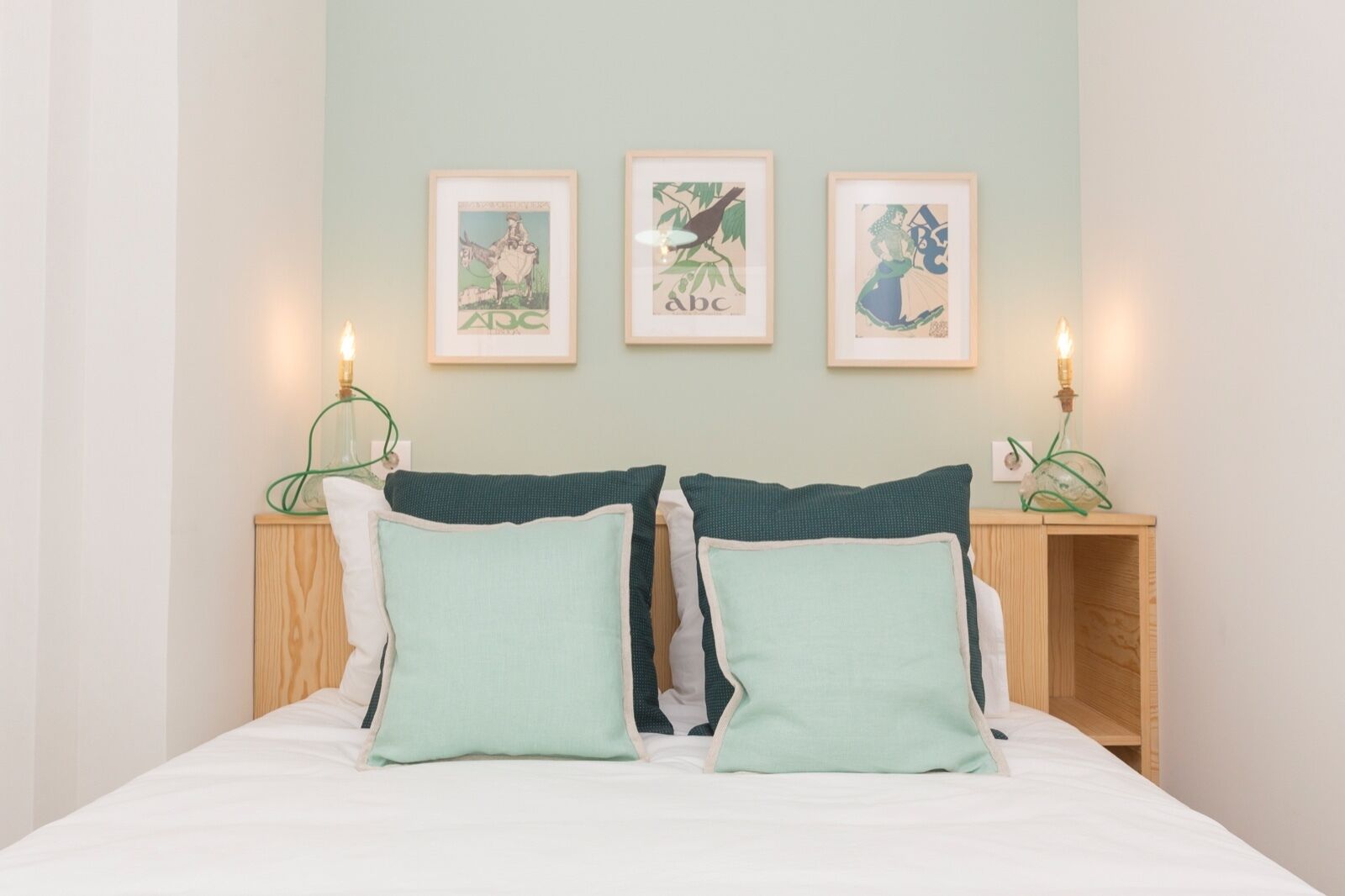 Une chambre à coucher avec un lit, deux tables de chevet et trois tableaux encadrés accrochés au mur.