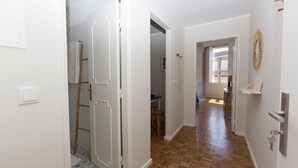 Un couloir doté d’un plancher en bois, de murs blancs et d’une porte donnant sur une pièce avec une fenêtre.