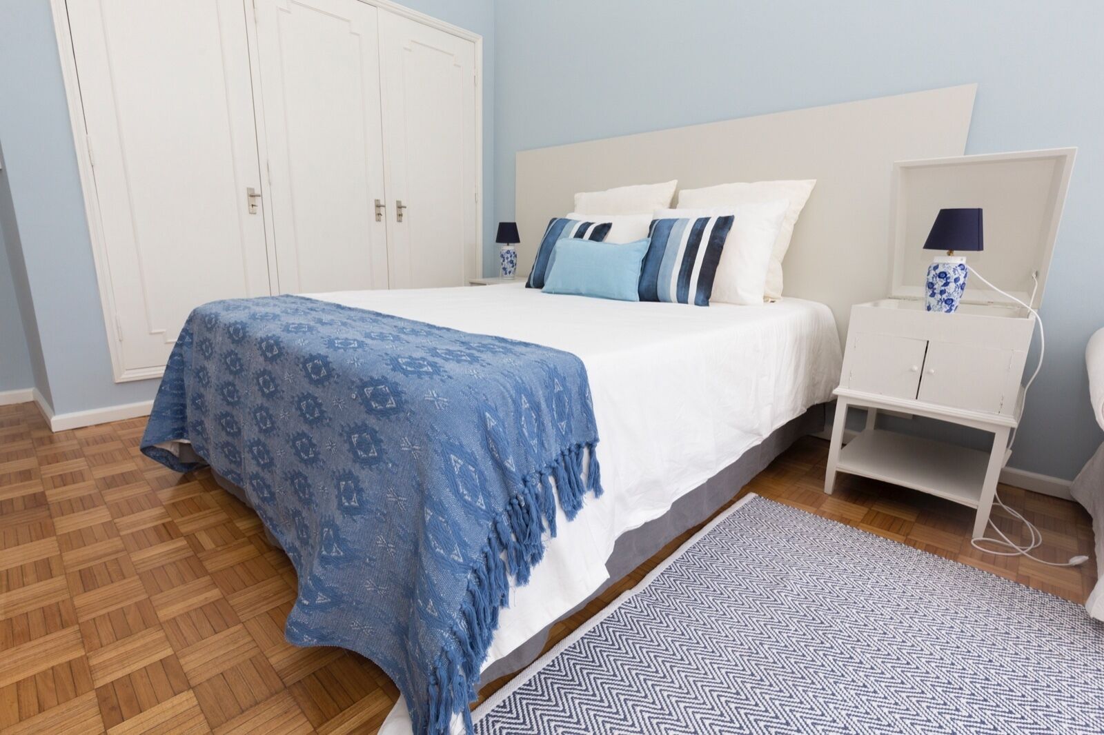 A bedroom with a bed, a nightstand, a wardrobe, and a patterned rug.