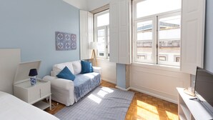 Une chambre moderne avec un lit blanc, une table de chevet blanche, un bureau avec un ordinateur, une fenêtre avec des volets blancs et un mur bleu.