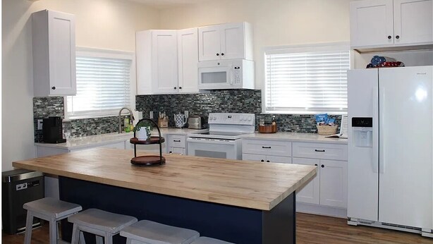 A modern kitchen with white cabinets, a central island with stools, a microwave, a stove, and a refrigerator.