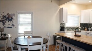 A modern kitchen with white cabinets, a wooden island, and a dining area with a round table and chairs.
