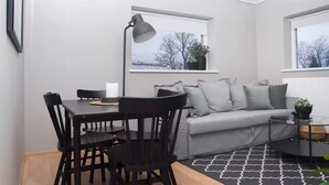A modern living room with a grey sofa, black chairs, a glass coffee table, and a large window with a view of trees. - Briet Apartments Akureyri, 2 bedroom (Akureyri)