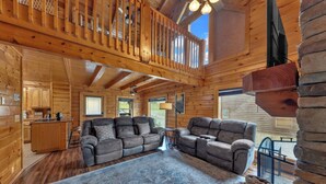 A spacious log cabin interior with a large living area, a kitchen, and a balcony with a wooden railing. - Bearly Behavin’ | Hot Tub, Pool, Arcade Game, MORE (Pigeon Forge)