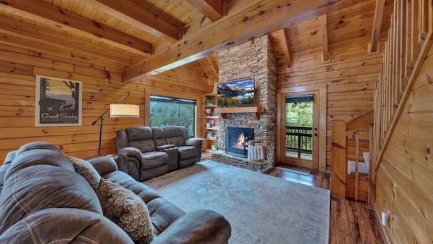 A log cabin interior with a stone fireplace, wooden ceiling beams, and a large sofa. - Bearly Behavin’ | Hot Tub, Pool, Arcade Game, MORE (Pigeon Forge)