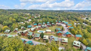An aerial view of a lodge with multiple cabins, surrounded by dense forest and a clear sky. - Bearly Behavin’ | Hot Tub, Pool, Arcade Game, MORE (Pigeon Forge)