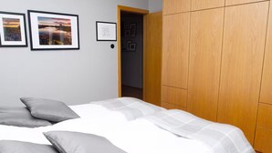 Ein Schlafzimmer mit einem Bett, grauen Kissen, einem Holzschrank und gerahmten Bildern an der Wand.