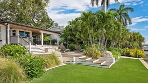 Een modern huis met een terras, tuinmeubilair en weelderige begroeiing.