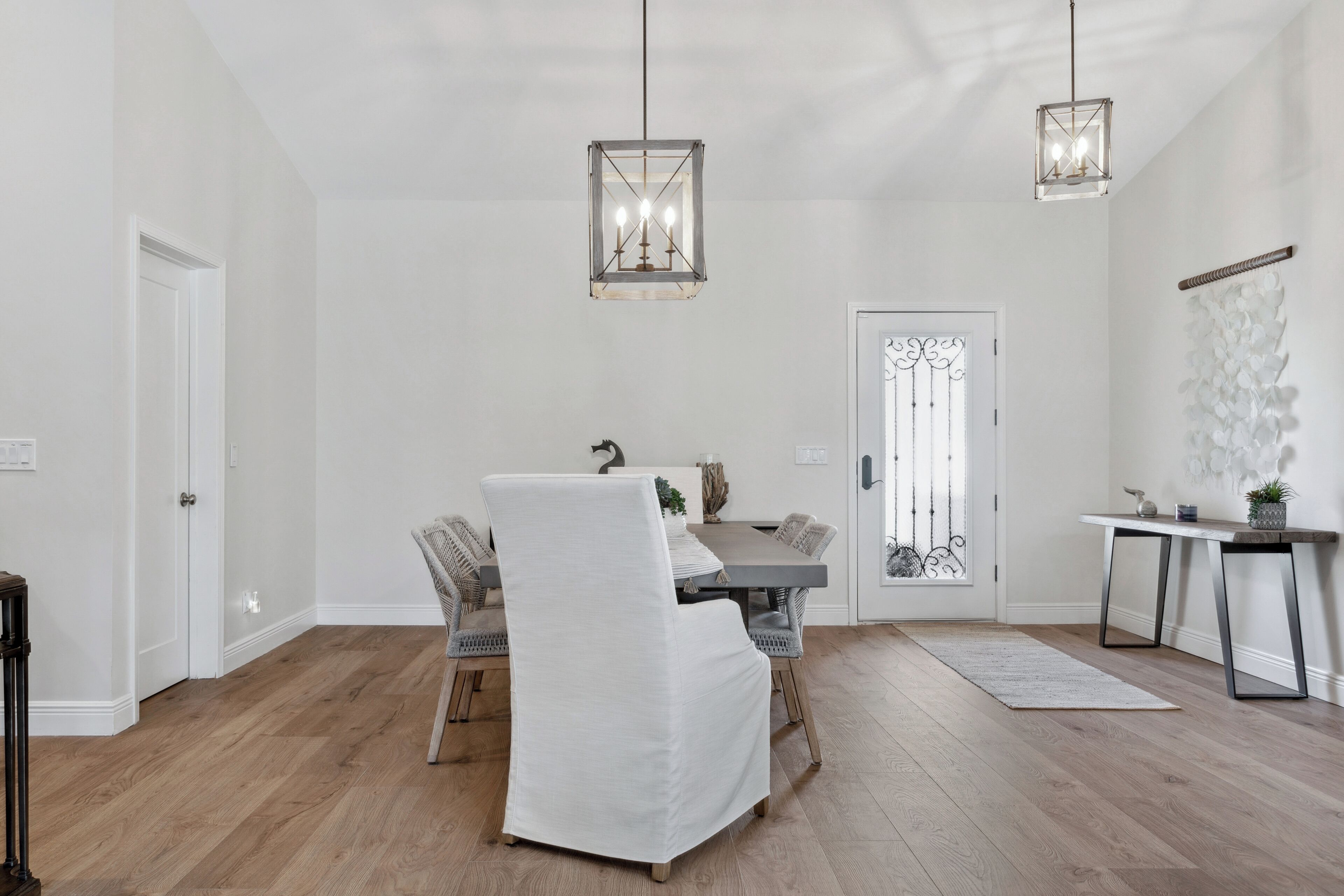 Un coin repas comprenant une chaise à revêtement blanc, une table à manger en bois et deux lampes suspendues.