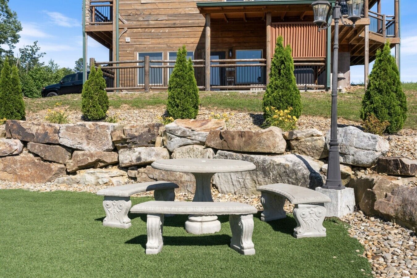 A stone picnic table with benches in front of a wooden building with a balcony.