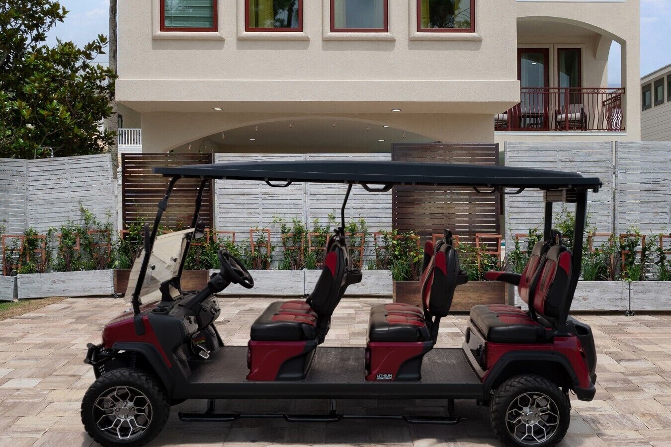 Un carrito de golf con tres asientos y un volante, estacionado frente a un edificio con balcón.