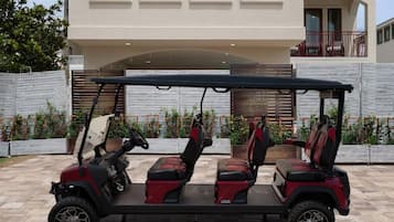 Un carrito de golf con tres asientos y un volante, estacionado frente a un edificio con balcón.