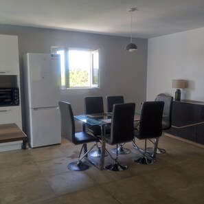 A compact kitchen with a dining table, chairs, a refrigerator, and a window. - A COMFORTABLE HOME (Allègre-les-Fumades)