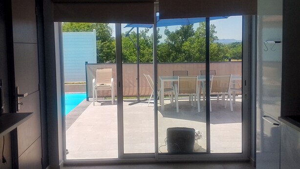 Une cuisine moderne avec une porte-fenêtre coulissante donnant sur un patio extérieur équipé d’une piscine et d’un espace salon.
