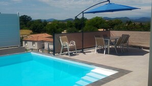 Une piscine à l’eau d’un bleu cristallin, entourée d’une terrasse carrelée, d’une chaise longue, d’une table et d’un parasol bleu.
