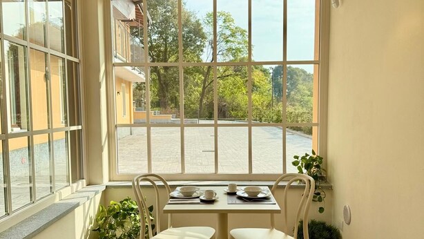 Un coin repas avec une table dressée pour deux personnes, de grandes fenêtres et une lampe suspendue.