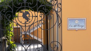 Une porte en fer forgé ornée d’un emblème représentant un lion, une enseigne indiquant « Ca’ del Borge », et un escalier menant à un bâtiment.