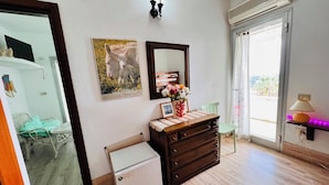 A room with a wooden dresser, a small refrigerator, a mirror, and a window with a view of palm trees.