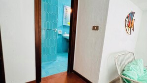A room with a wooden floor, a white chair, and a blue-tiled bathroom visible through an open door.
