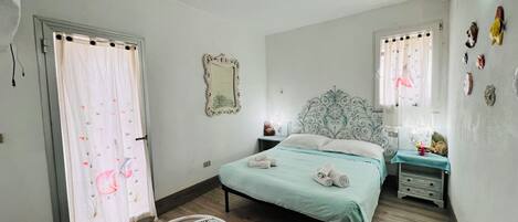 A bedroom with a bed, a chair, a bedside table, a nightstand, and a wall-mounted air conditioner.