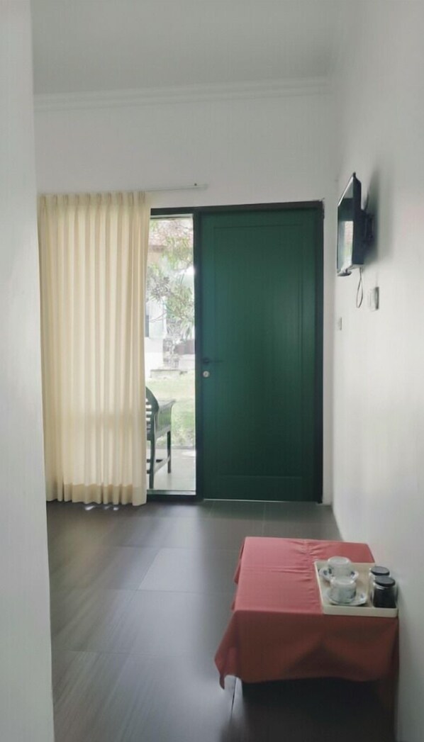A room with a green door, a table with a red tablecloth, and a TV mounted on the wall. - La Plage Beach Club & Resort (Cikakak)