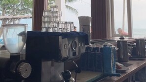 A kitchen area with a coffee machine, a large window with a view of palm trees, and a wooden counter with various items. - La Plage Beach Club & Resort (Cikakak)