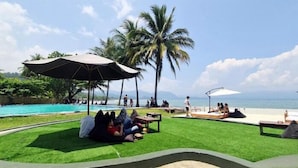 A poolside area with artificial grass, palm trees, and umbrellas. - La Plage Beach Club & Resort (Cikakak)
