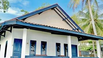 Una casa de dos pisos con fachada azul y blanca, tejado de tejas y un balcón con barandilla azul.