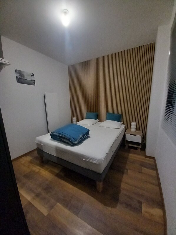 A bedroom with a bed, a bedside table, a wall-mounted picture, and a window with blinds.