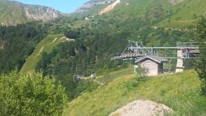 Un paisaje montañoso con un sistema de teleférico, un edificio pequeño y abundante vegetación.