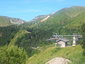 A mountain landscape with a cable car system, a small building, and lush greenery. - 'Au Petit Bonheur T2 4 Guests' Apartment with Mountain View and Unlimited Wi-Fi (Mont-Dore)