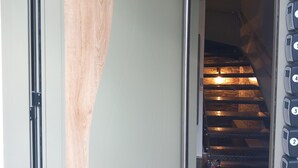 Un pasillo con una puerta corredera, una escalera con acabado de madera y una pared con botones de llamada numerados.