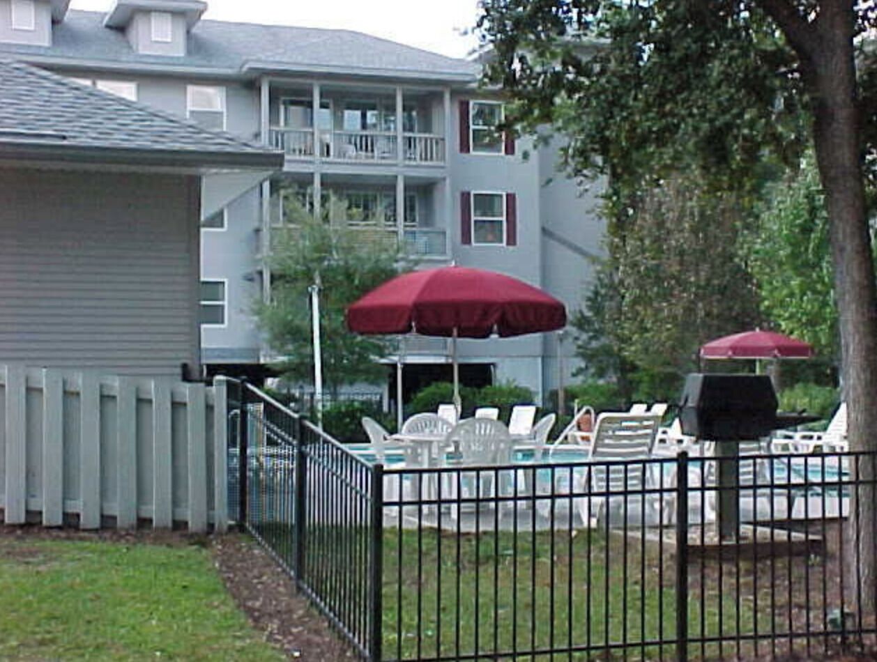 En bostadsfastighet med en inhägnad trädgård, en swimmingpool och utomhusmöbler under parasoller.