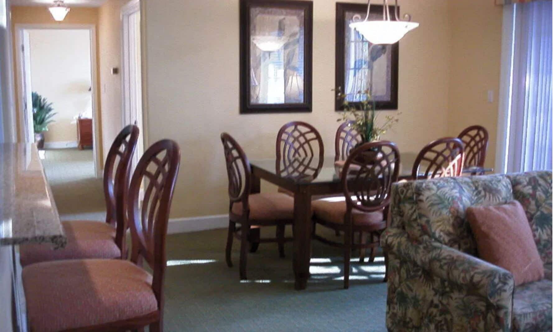 A dining area with a round table and chairs, a patterned sofa, and two framed pictures on the wall.
