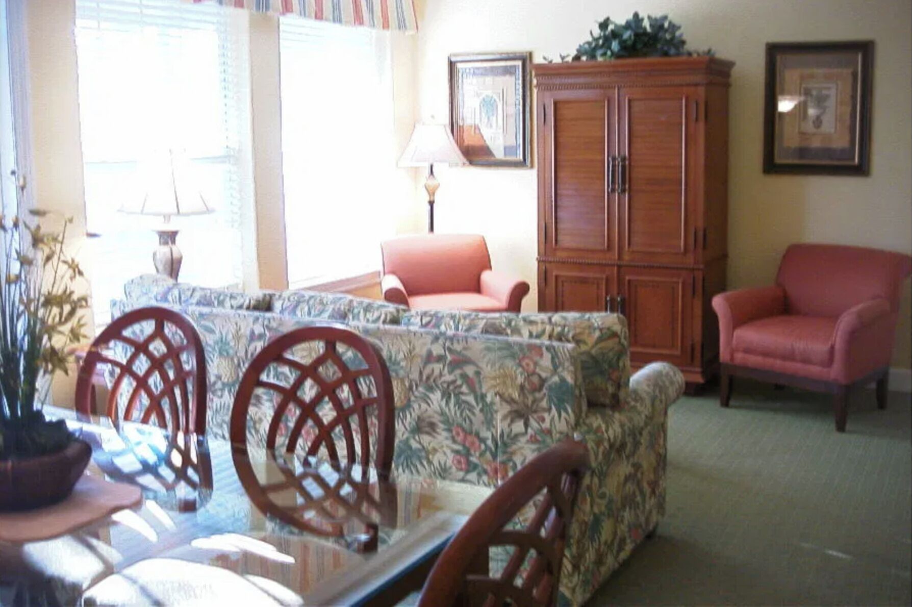 A living room with a sofa, two chairs, a wooden cabinet, and a table with a lamp.