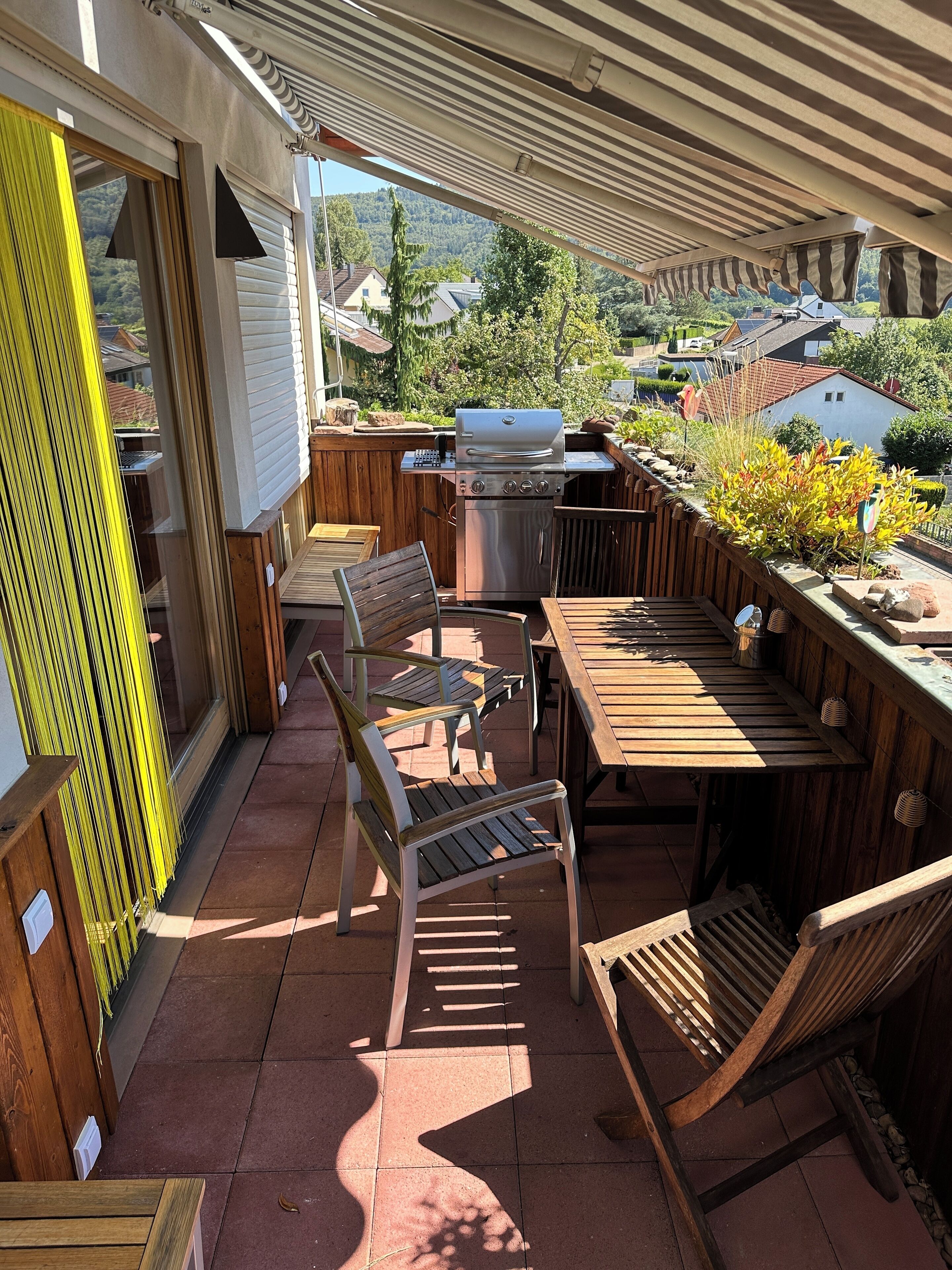 Un patio al aire libre con mobiliario de madera, una parrilla y vista a una zona residencial.