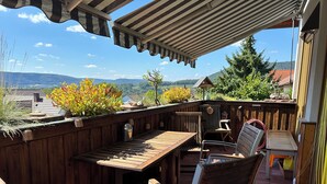 A wooden deck with a table and chairs, overlooking a scenic view of mountains and houses. - FEWOBuergstadt.de Light-flooded, cozy, spaciousFeWo with distant view (Bürgstadt)