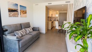 Ein modernes Wohnzimmer mit grauem Sofa, einem Esstisch mit Stühlen und einer Küche im Hintergrund.