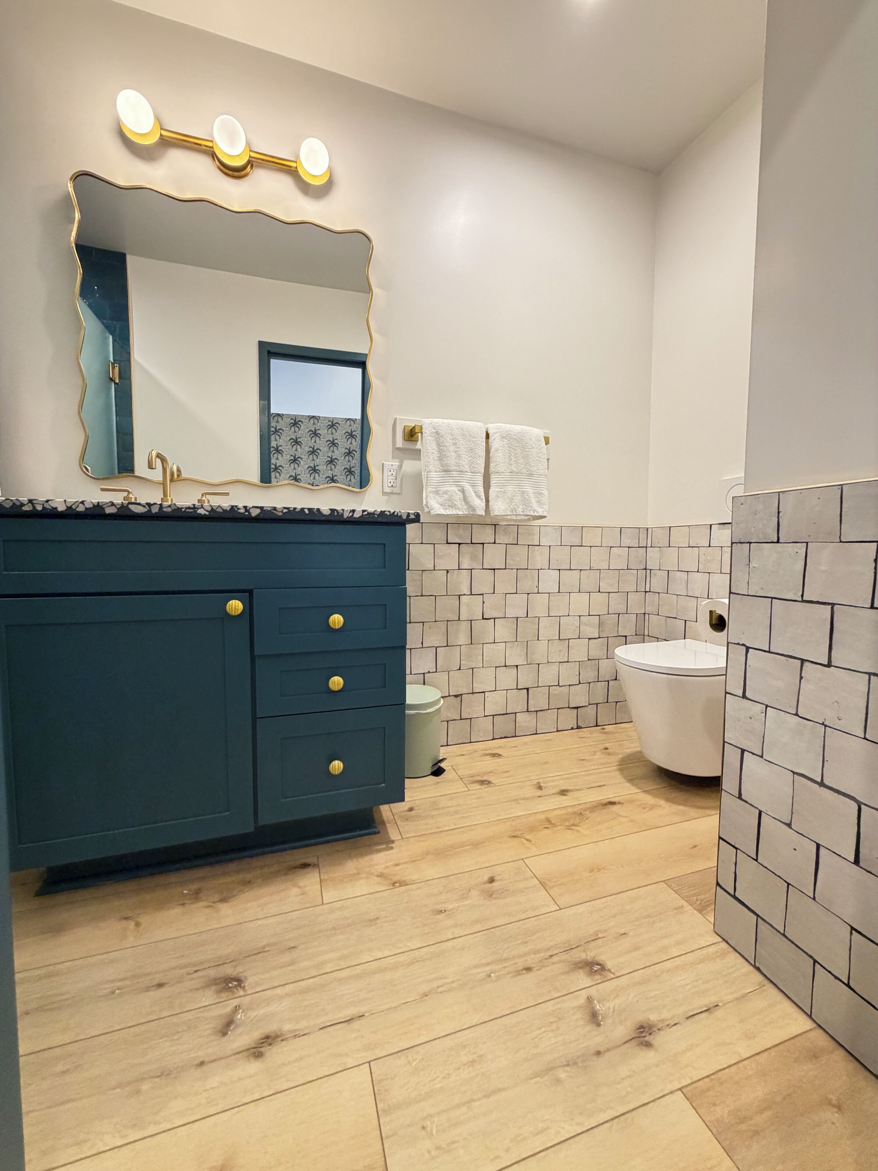 A bathroom with a dark blue vanity, a white toilet, and a tiled wall.