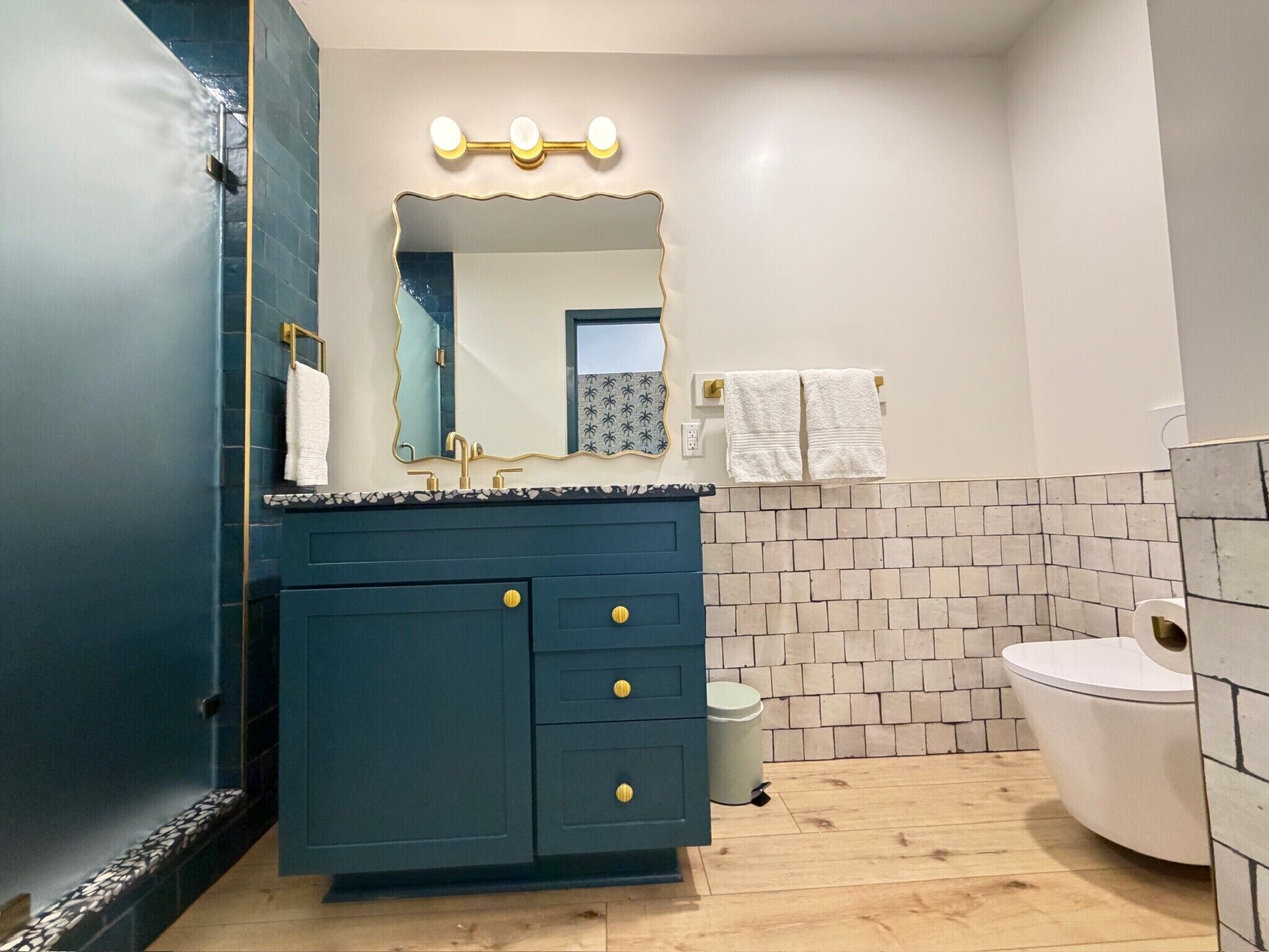 Une salle de bain avec un meuble-lavabo bleu foncé, des toilettes blanches et un miroir surmonté de luminaires.
